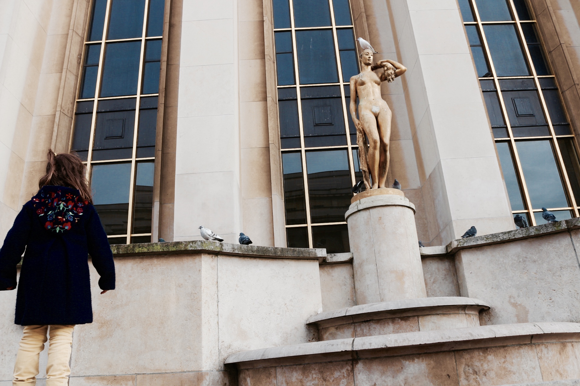 A girl standing in front of female status with pigeons